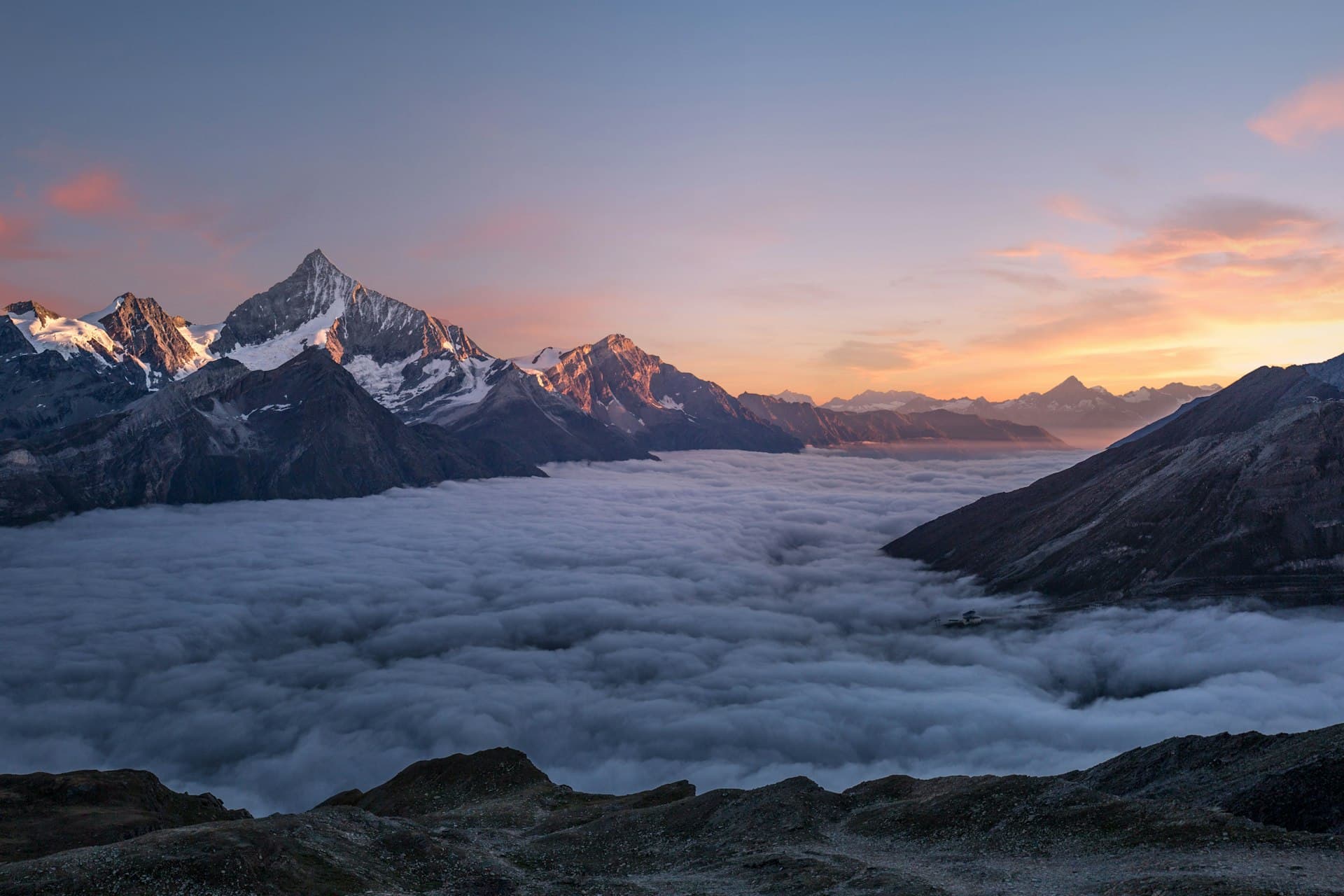 Mountain peaks rising above a sea of clouds at sunset